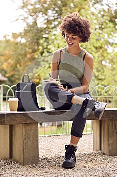 Young Woman Outdoors In Park Sitting On Bench Working Writing In Notebook 