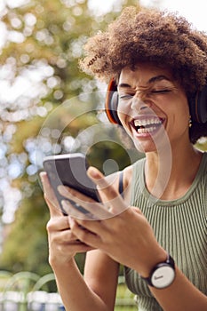 Young Woman Outdoors Wearing Wireless Headphones Streaming Show From Mobile Phone 