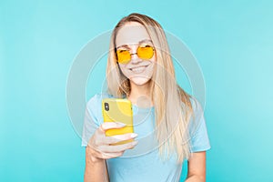 Young woman over isolated blue background reading a sms message and smiles. Positive emotions