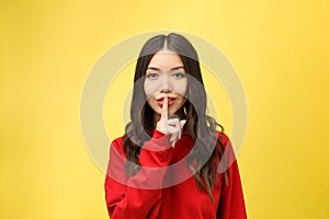 Young woman over yellow wall showing a sign of silence gesture putting finger in mouth
