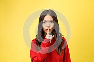 Young woman over yellow wall showing a sign of silence gesture putting finger in mouth