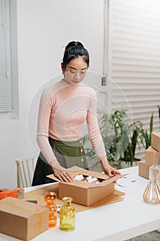 Young woman, owener of small business packing product in boxes, preparing it for delivery