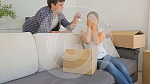 Young woman packing things in boxes. Man enters the room and giving her keys from new house.