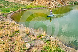 Young woman on paddle board SUP at lake Iacobdeal, Romania, paddling near the shoreline, on tranquil, pristine waters, at sunset