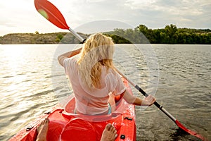 Young Woman Paddling Kayak on the Beautiful River or Lake at Sunset. Back View from the Second Place in Boat.