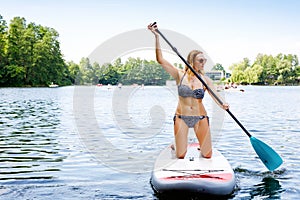 Young woman paddling on sup board on a lake. Active woman on modern trendy stand up paddle board. Summer outdoors