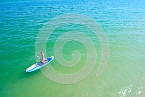 Young woman paddling on SUP board on the tropical beach. Active summer vacations with paddle board.