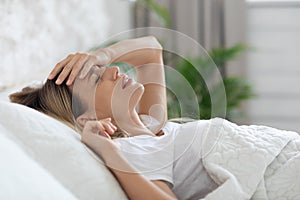 Young woman in pain laying in bed, toching her head
