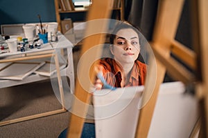 Young woman painter sitting in front of the canvas and drawing. Working in artist studio. Creative concept