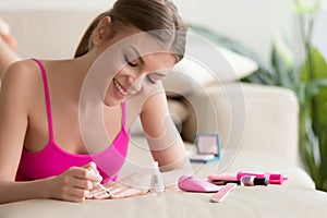 Young woman painting nails with varnish at home