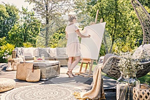 Young woman painting on a white canvas on a sunny terrace with g