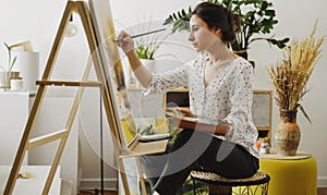 A young woman paints in her apartment with oil paints. Female student draws in art studio.Fine art study concept.