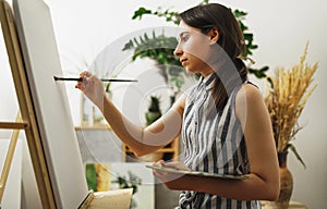 A young woman paints in her apartment with oil paints. Female student draws in art studio.Fine art study concept.