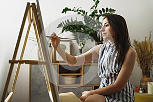 A young woman paints in her apartment with oil paints. Female student draws in art studio.Fine art study concept.