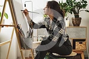 A young woman paints in her apartment with oil paints. Female student draws in art studio.Fine art study concept.mockup