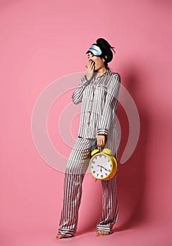 Young woman in pajama just after sleep woke up with sleepy bandage mask hold yellow alarm clock