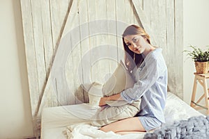 Young woman in pajama wake up in the morning in cozy scandinavian bedroom and lying on bed with oversize knitted blanket