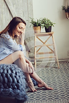 Young woman in pajama wake up in the morning in cozy scandinavian bedroom and lying on bed with oversize knitted blanket