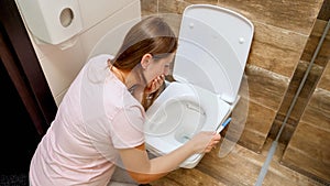 Young woman in pajamas feeling sick vomitting in toilet after doing pregnancy test. Intoxication and nausea during