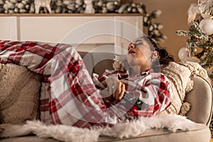 A young woman in pajamas fell asleep on the sofa in front of the TV while watching the Christmas broadcast