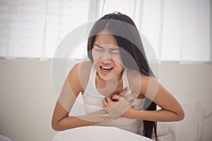 Young woman in pajamas having heart attack in bed