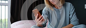 Young woman in pajamas sitting in bed with mobile phone in hand