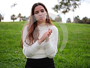 A young woman in the park condescendingly clapping to camera.