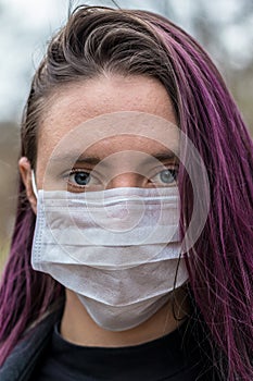 Young woman in park in a light, soft protective medical mask for face protection against virus outbreak, close up portrait