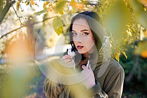 Young woman in park on sunny autumn day. Cheerful beautiful female in jacket with a hood outdoors on beautiful fall day