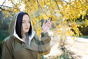 Young woman in park on sunny autumn day. Cheerful beautiful female in jacket with a hood outdoors on beautiful fall day