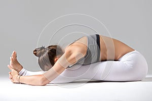 Young woman in paschimottanasana pose, grey studio background