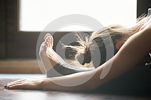 Young woman in paschimottanasana pose, home interior background,