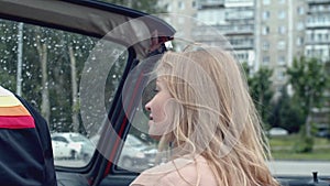 Young woman on passenger seat in a cabriolet car. Stock. Rain drops on car windshield and summer city on the background.