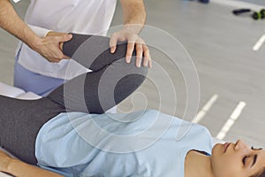 Young woman patient lying and getting procedure of knee and leg joints from chiropractor