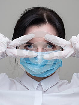 Young woman patient in a medical mask puts on protective surgical sterile gloves on her arm, on gray background, protection