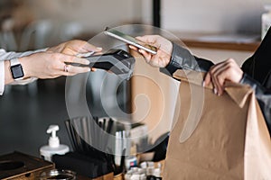 Young woman paying bill through smartphone using NFC technology in a cafe. Female customer paying using contactless