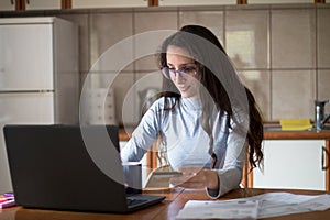 Young woman paying bills with debit card from home