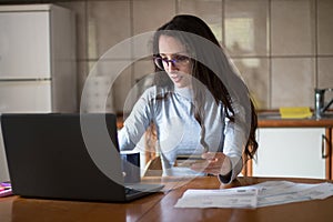 Young woman paying bills with debit card from home