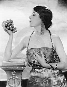 Young woman in pearls and elegant dress holding and looking at grapes