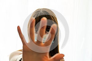 Young woman peeking through fingers while signaling to stop with hand while wearing face mask