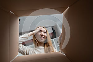 Young Woman Peeking Inside Cardboard Box With Curiosity photo