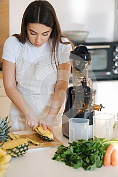 Young woman peel ananas on wooden table. Preparing fruits for homemade juice. Vegan beverage
