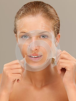 Young woman peeling off a facial mask smiling