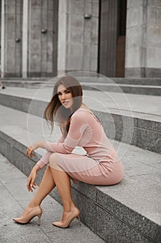 Young woman with a perfect body and long sexy legs in beige tight dress and trendy shoes posing at urban background