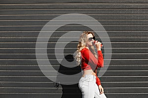 A young woman with a perfect body in a red sweatshirt is drinking cool soft drink on a summer sunny day outdoors.