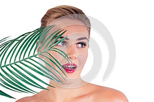 Young woman perfect skin make-up with long eyelashes and red lipstick holding a tropical palm leaf closeup shoulders