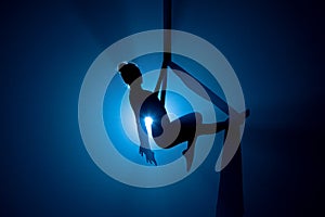 A young woman performing in a circus on aerial silk in the dark with blue light. Silhouette of female equilibrist