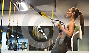 Young woman performing TRX training in gym, copy space