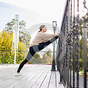 A young woman performs an exercise to stretch the muscles of her legs, placing one leg on the railing