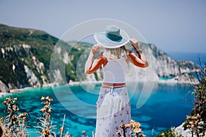 Young woman on Petani beach Kefalonia, holding blue sunhat enjoying picturesque panorama of emerald azure bay lagoon